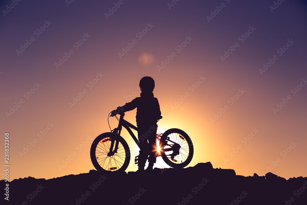 Fototapeta premium Silhouette of a little girl with a bicycle at sunset