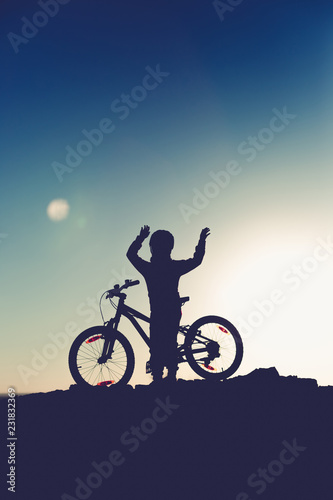 Fototapeta Naklejka Na Ścianę i Meble -  Silhouette of a little girl with a bicycle at sunset