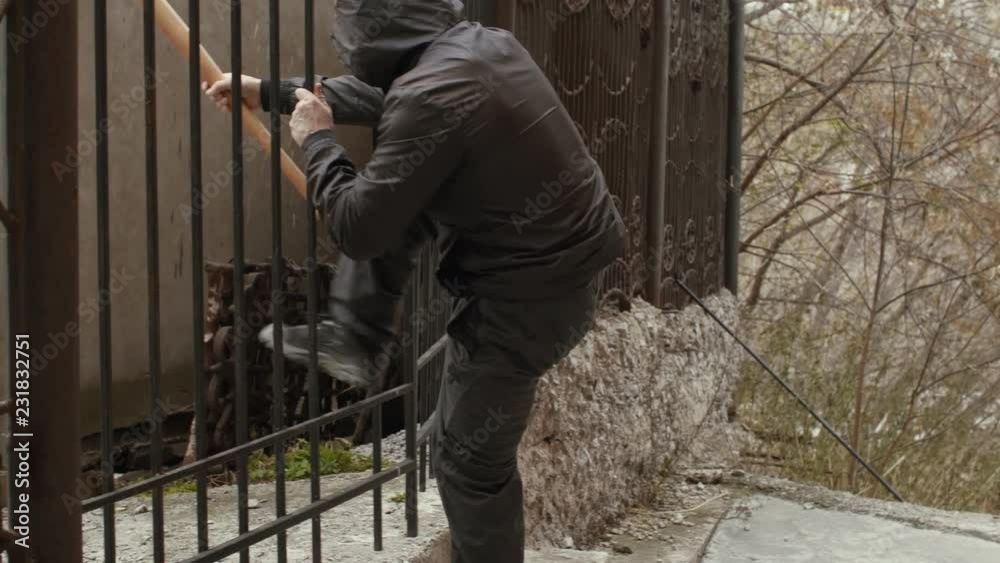 Robber in mask holding bat and sliping through the fence Robber in mask holding bat and sliping through the fence