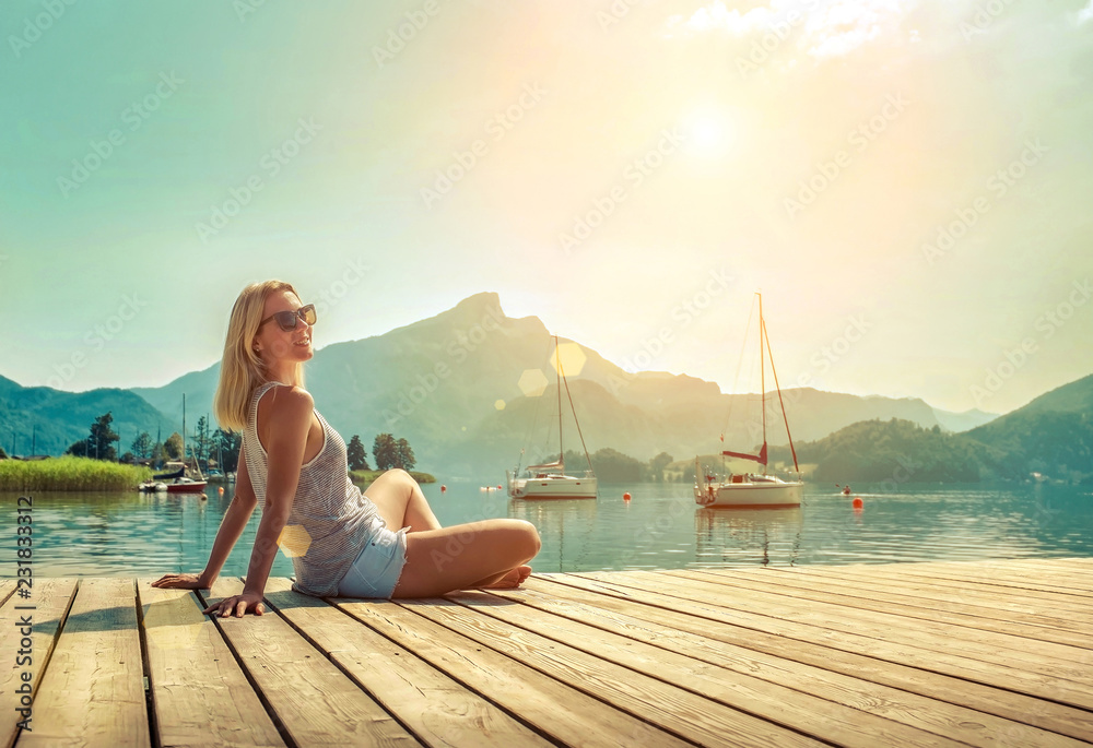Happiness blonde woman seat on the wooden pier near the mountain