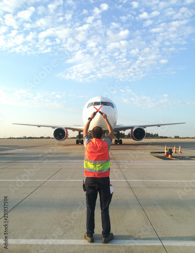 Ground Crew in the signal vest. Aviation Marshall / Supervisor meets passenger airplane at the airport. Aircraft is taxiing to the parking place.