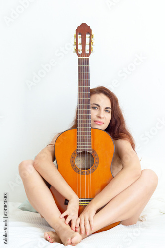 Happy young nude woman sitting on her bed and hugging an acoustic guitar. Sex and music. Concept muse. Love is like art.