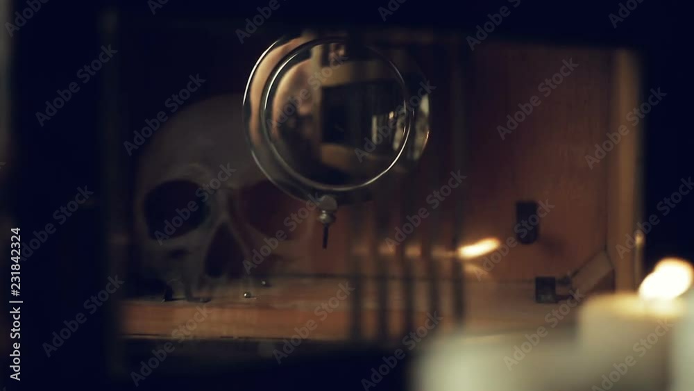 reflection of the skull and candles in the pendulum of an old clock