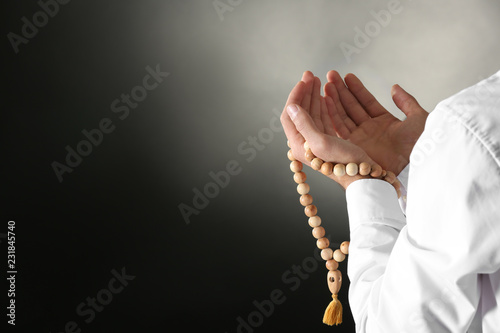 Young Muslim man with rosary beads praying on dark background, closeup photo