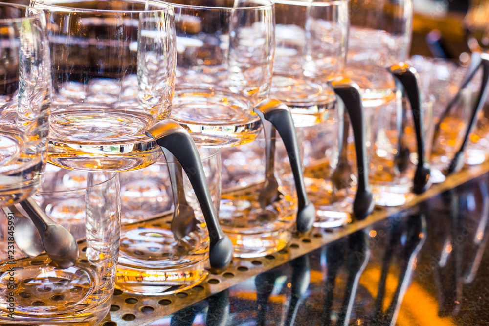 Transparent glasses for alcoholic beverages stand on the bar with a spatula. Yellow lights on the bar, the table reflects the glasses. Service in a restaurant or bar Transparent glasses for alcoholic beverages stand on the bar with a spatula. Yellow lights on the bar, the table reflects the glasses. Service in a restaurant or bar