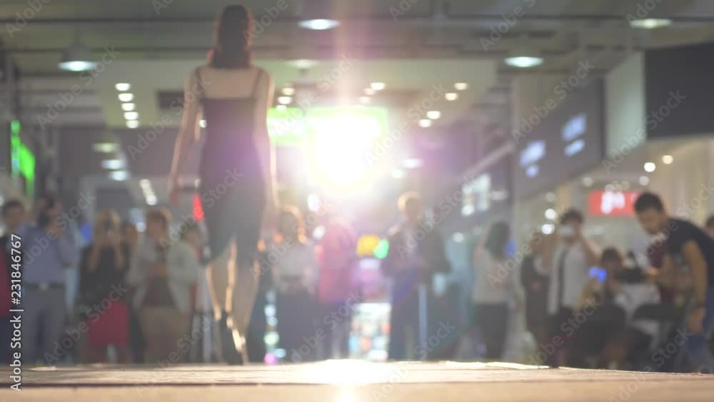 slim professional model in a black dress on high heels defiles the podium in backlight during a fashion show