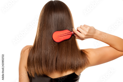 Back view of young woman combing her long hair on white background