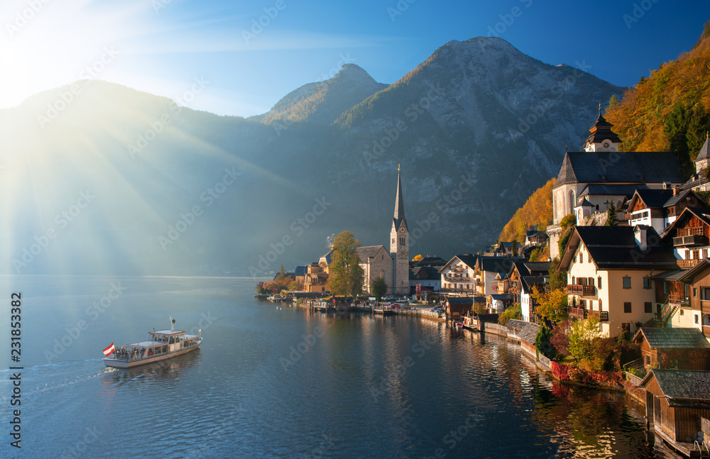 Scenic view of famous Hallstatt mountain village in the Alps with traditional passenger ship at autumn morning