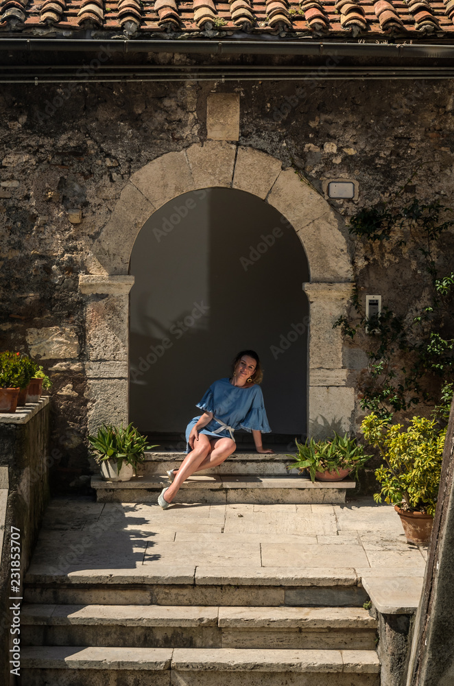 A young girl sits on the steps near the entrance to an old antique house in a small Italian town