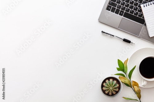 White desk copy space seen from above with a laptop keyboard, notebook, coffee, pen, cactus and green dried leaves