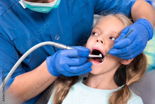 cropped shot of dentist with dental handpiece working with teeth of little child
