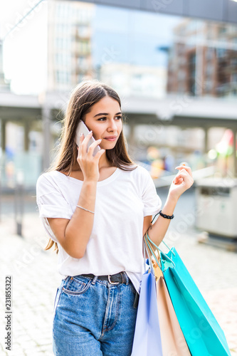 Young woman walking at the street with shopping bags talking on mobile phone