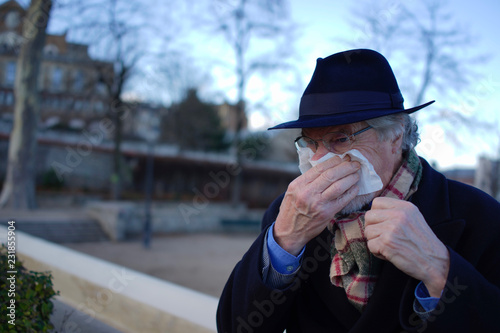 Foto Old man with cold or flu blowing nose with kleenex tissue handkerchief outside i