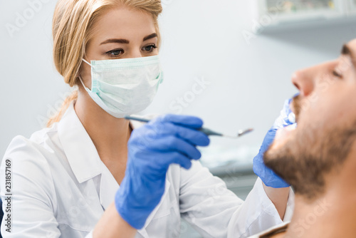young female dentist examining teeth of handsome smiling client
