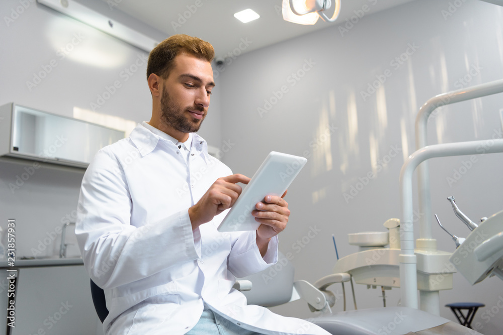 Fototapeta premium bottom view of attractive young dentist in coat using tablet in office