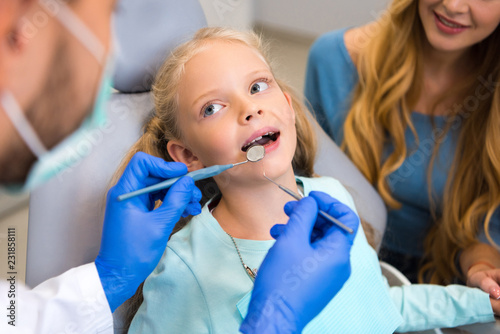 cropped shot of dentist working with adorable little child while young mother sitting near her for support