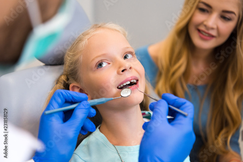 cropped shot of dentist working with little child while young mother sitting near her for support