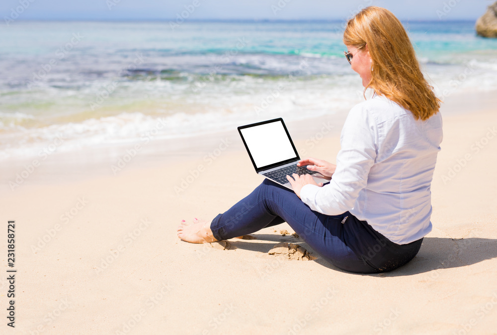 Woman working on computer while relaxing on the beach