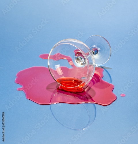 A glass and spilled liquor on a light blue background. Art photo..