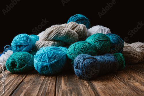 close up view of white, blue and green yarn for knitting on wooden surface on black backdrop