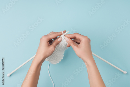 Картината върху платно partial view of woman with white yarn and knitting needles knitting on blue back