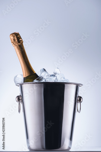 close up view of bottle of champagne in bucket with ice cubes on grey background