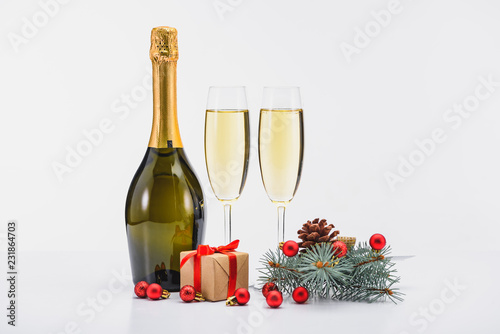close up view of bottle and glasses of champagne, christmas decorations and present on white background