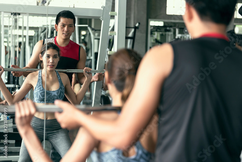 Trainer with asian woman lifting barbell in gym. healthy lifestyle and workout motivation concept.