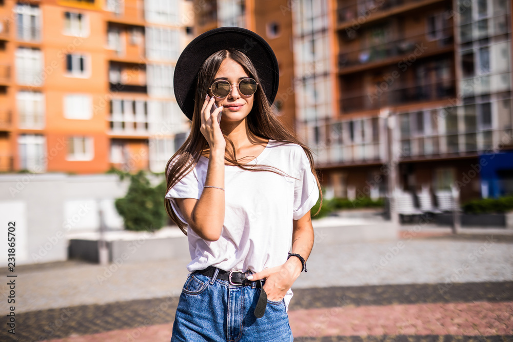 Fototapeta premium Beautiful young trendy woman in sunglasses and hat while talking on the phone on sunny day
