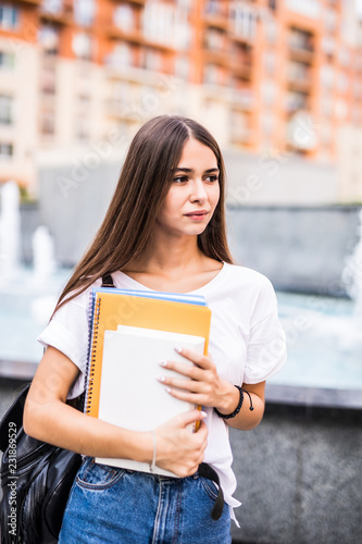 Portrait of a serious student woman holding folders walking looking away in the street