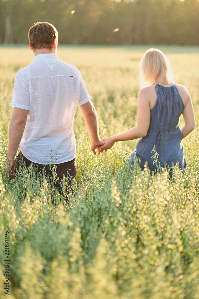 The couple go on a field at sunset holding hands, green tall grass The couple go on a field at sunset holding hands, green tall grass