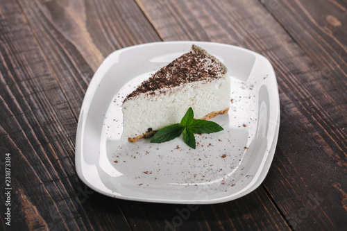 White cheesecake with cacao topping and mint served on a white plate.