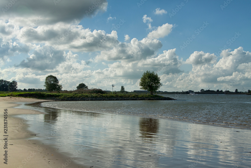 Dutch landscape with blue sky and clouds, horizon and river with sand coast, canal, tree, wind mill, beach