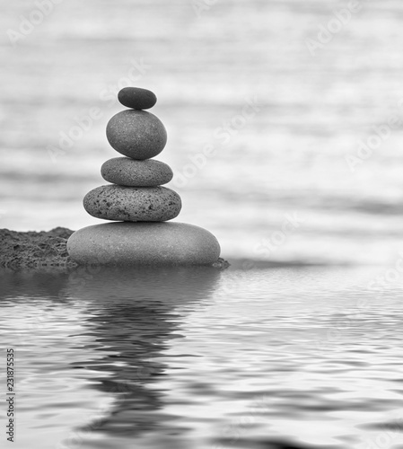 balanced pebble stack reflecting on calm water in black and white colors