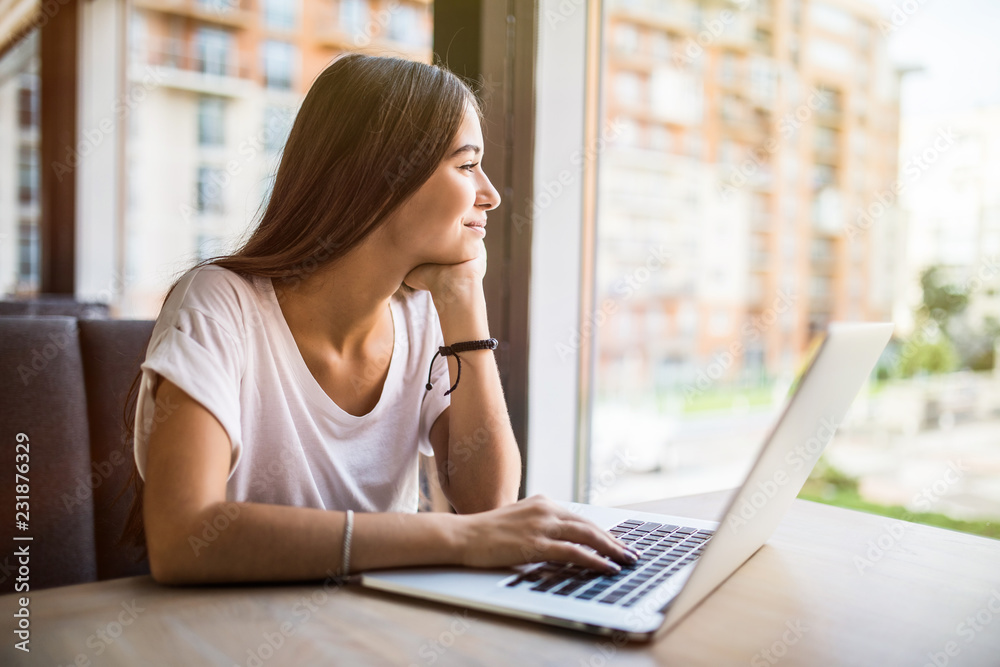 Charming thoughtful girl looking out of window and thinking on creative ideas for developing own training project sitting at laptop in coffee shop Charming thoughtful girl looking out of window and thinking on creative ideas for developing own training project sitting at laptop in coffee shop