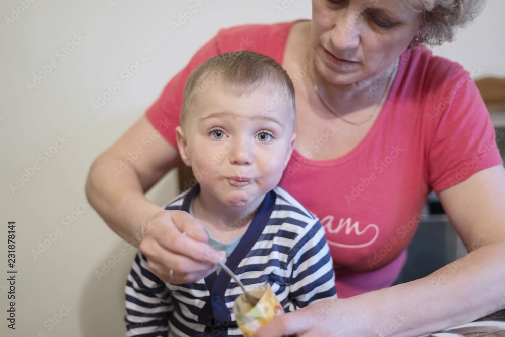 Woman feeding with a spoon a little boy, 1.5 years old, in the home