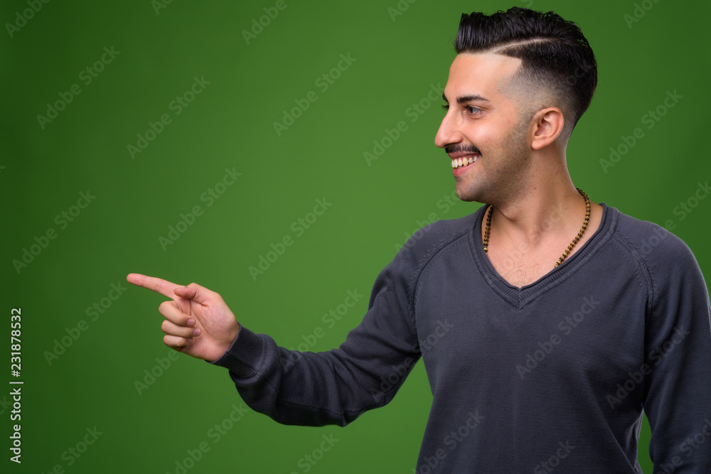 Young handsome Iranian man with mustache against green backgroun