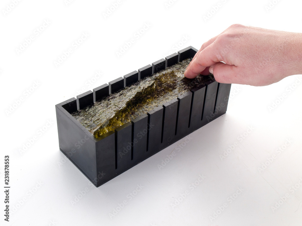 Caja para cortar suhis finalizando la introducción de algas en ella sobre un fondo blanco Caja para cortar suhis finalizando la introducción de algas en ella sobre un fondo blanco