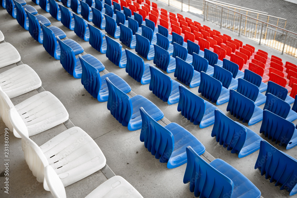 Naklejka premium Empty white, red and blue rows of plastic seats on the concrete bases of the sports building, stadium