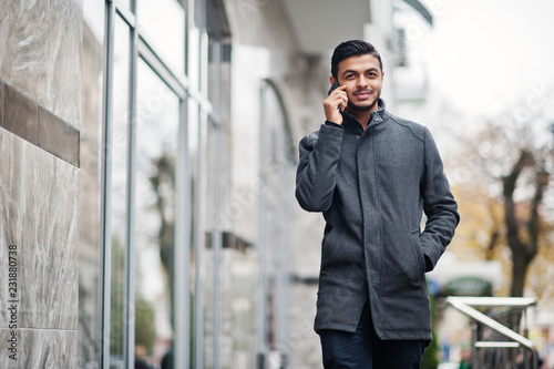 Stylish indian hindu man in gray coat posed on street and speaking at phone.