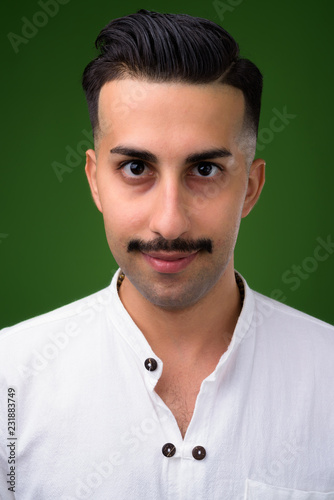 Young handsome Iranian man with mustache against green backgroun