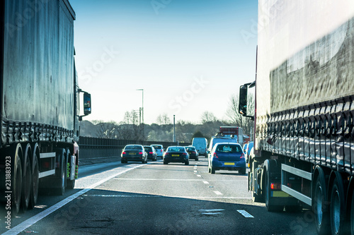 Closeup of two big trucks next to each other in busy Highway transportation motorway full of cars in the evening with dark blue sky