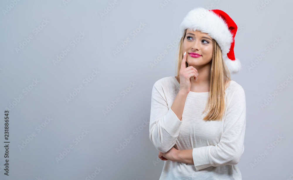 Young woman with Santa hat thoughtful pose on a gray background Young woman with Santa hat thoughtful pose on a gray background