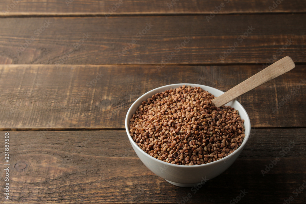 Dry buckwheat groats in a white bowl with a spoon on a wooden brown table. cereals. healthy food. porridge. Dry buckwheat groats in a white bowl with a spoon on a wooden brown table. cereals. healthy food. porridge.