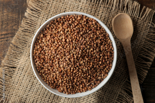 Dry buckwheat groats in a white bowl with a spoon on a wooden brown table. cereals. healthy food. porridge. top view