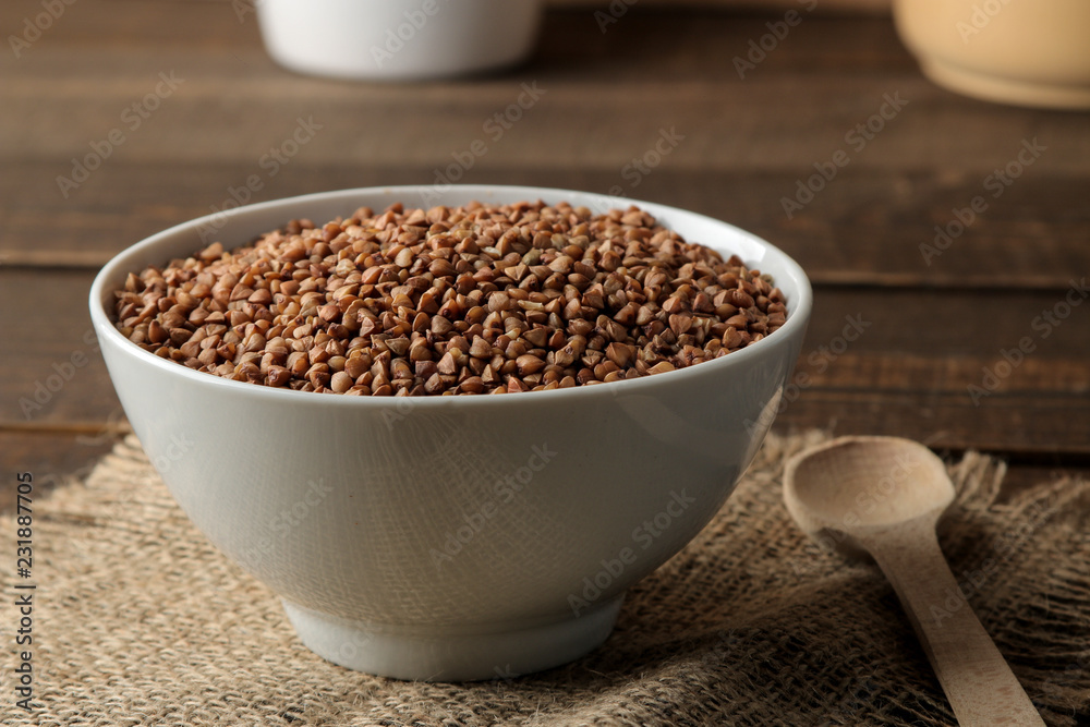 Dry buckwheat groats in a white bowl with a spoon on a wooden brown table. cereals. healthy food. porridge. Dry buckwheat groats in a white bowl with a spoon on a wooden brown table. cereals. healthy food. porridge.
