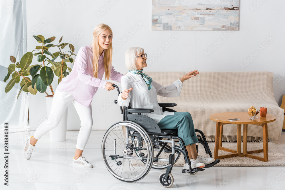 young woman pushing wheelchair with happy senior woman in nursing home young woman pushing wheelchair with happy senior woman in nursing home