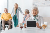 senior woman holding digital tablet at nursing home with senior people and doctor at background