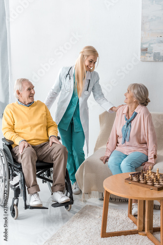 young cheerful female doctor talking to senior people at nursing home