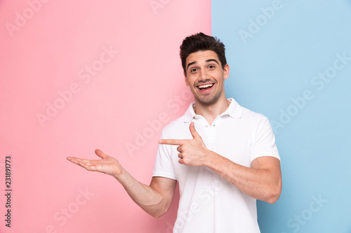 Image of handsome man 30s having stubble pointing fingers aside at copyspace, isolated over colorful background